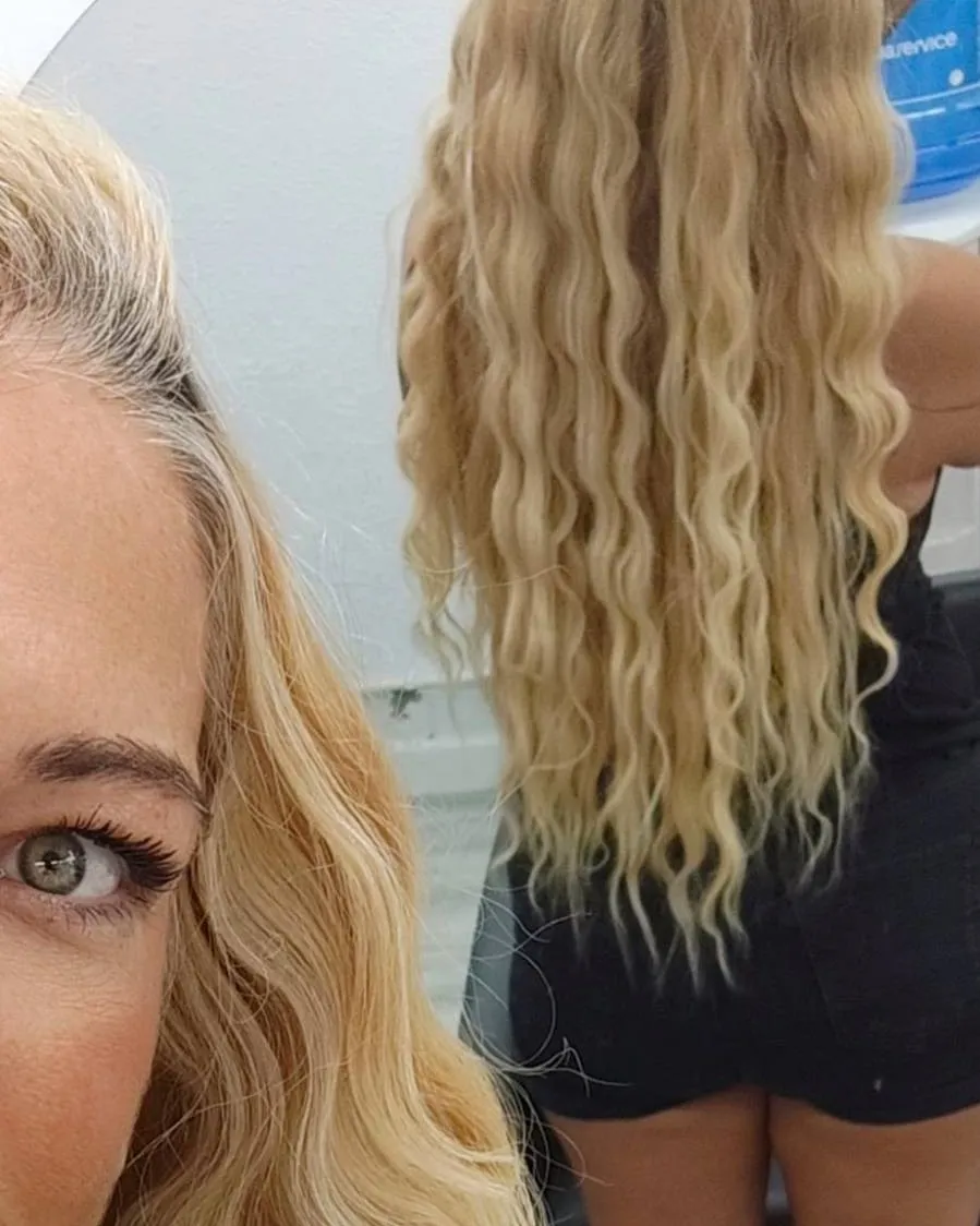 Melena rubia larga con ondas marcadas, reflejada en el espejo del salón